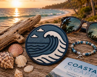 May include: A circular embroidered patch featuring a dark blue ocean wave design with white foam details. The patch is displayed alongside seashells, a beaded bracelet with a wave charm, sunglasses, and a book titled Coastal Escapes.