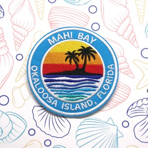 May include: A blue and white embroidered patch with the text "Mahi Bay Okaloosa Island, Florida" and a sunset scene with palm trees.