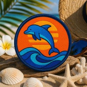 May include: Round patch featuring a blue dolphin leaping over waves, set against an orange sunset. The patch has a blue border. The design evokes a beach theme, with a seashell and starfish in the background.