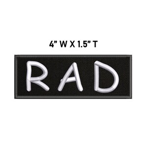May include: A rectangular embroidered patch with a black background and the white text RAD in a sans-serif font. The patch features a black border and measures 10.16 cm wide by 3.81 cm tall as indicated by the text above the item.