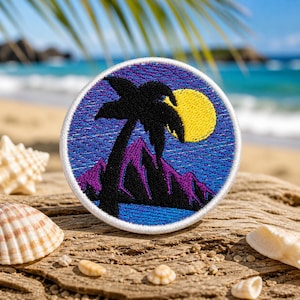 May include: Embroidered patch featuring a tropical beach scene. The design includes a black palm tree, purple mountains, and a yellow moon against a blue and purple sky. The patch has a white border and is set on a wooden surface with seashells.
