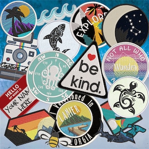 May include: A collection of colorful embroidered patches with various designs, including a compass, a turtle, a mountain, a camera, a palm tree, a whale, and a compass. The patches have a variety of text, including "Explore", "Not All Who Wander", "Be Kind", "Hello My Name Is", "Your Name Here", "Lanier", and "Georgia".