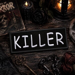 Pode incluir: Um emblema retangular bordado em preto com a palavra KILLER em letras maiúsculas brancas em negrito. O emblema tem uma borda costurada limpa e é apresentado na orientação horizontal, exibindo um design de alto contraste e tipografia clara.