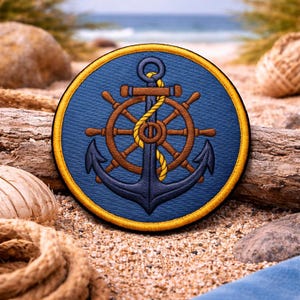 Puede incluir: Un parche redondo azul marino con un diseño náutico. Presenta un timón y un ancla marrones, con una cuerda amarilla. El diseño está sobre un fondo azul y tiene un borde dorado. Ideal para entusiastas marítimos.
