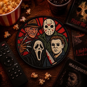 May include: A circular embroidered patch featuring four horror movie characters: a man in a brown fedora with clawed hands, a hockey mask-wearing figure, a ghost-faced figure in a black hood, and a man with a knife against a red sunburst background.