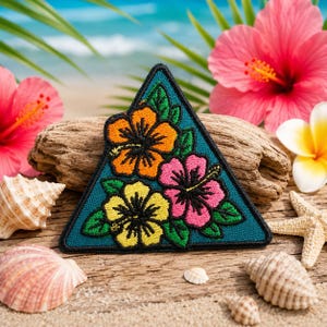May include: A teal triangular patch with embroidered hibiscus flowers in orange, pink, and yellow, with green leaves and black outlines. The patch is set against a beach scene with seashells, starfish, and tropical flowers.