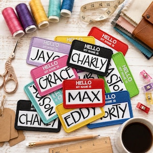May include: A collection of rectangular embroidered name patches in various colors, each featuring the text HELLO MY NAME IS and a custom name. The patches are scattered alongside sewing supplies including thread spools, a measuring tape, and scissors.