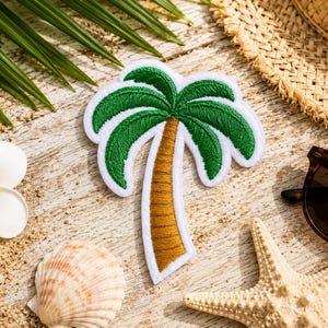 May include: Embroidered palm tree patch with green fronds and a brown trunk, outlined in white. The patch is on a sandy surface with a seashell, starfish, sunglasses, and a straw hat, evoking a tropical theme.
