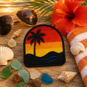 May include: A semi-circular embroidered patch featuring a sunset gradient of red, orange, and yellow above a black silhouette of a palm tree and rolling hills, with two thin blue wavy lines representing water at the base of the landscape.