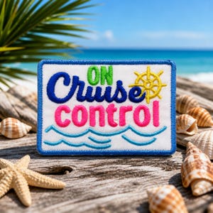 May include: Embroidered patch with the words "ON Cruise Control" in blue, green, and pink. A yellow ship's wheel is on the right. The patch is on a wooden surface with seashells and a starfish, with a beach and ocean in the background.