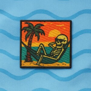 May include: Embroidered patch featuring a skeleton relaxing in a hammock on a beach. The design includes a palm tree, sunset, and the skeleton wearing sunglasses. The patch has a black border and is set against a blue background with wave patterns.