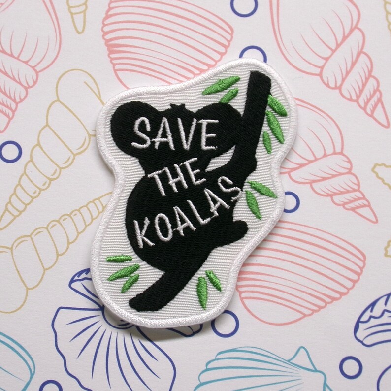 May include: Black and white embroidered patch of a koala holding onto a branch with green leaves. The text "SAVE THE KOALAS" is embroidered in white on the patch.