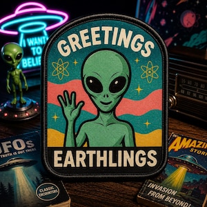 May include: A rectangular patch with rounded corners featuring a green alien waving. The text GREETINGS EARTHLINGS is printed in white. The background consists of wavy teal, pink, and yellow stripes with yellow atom symbols and stars.
