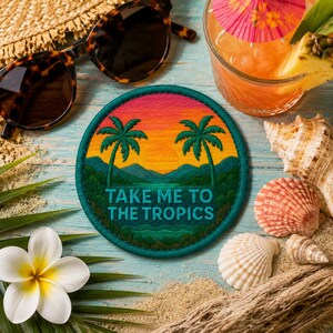 May include: A circular embroidered patch featuring a tropical sunset scene with two palm trees, mountains, and the text "TAKE ME TO THE TROPICS" in teal lettering. The patch has a dark teal border and is surrounded by sunglasses, a drink, and shells.