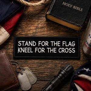 May include: A rectangular black embroidered patch featuring the white text STAND FOR THE FLAG KNEEL FOR THE CROSS. The patch is surrounded by a brown leather wallet, metal dog tags, a black flashlight, a Holy Bible, and a folded American flag.