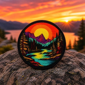 Puede incluir: Parche bordado redondo que representa una puesta de sol sobre un paisaje montañoso con un río. El diseño incluye un sol amarillo, montañas moradas y árboles coloridos. El parche tiene un borde negro y está sobre un fondo natural.