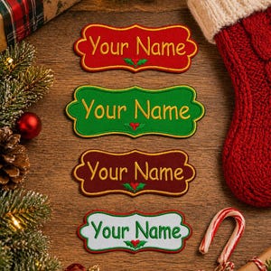 Puede incluir: Cuatro parches bordados con el texto "Your Name" en rojo, verde, marrón y blanco. Cada parche presenta un diseño de hoja de acebo. Calcetín navideño y caja de regalo en el fondo.