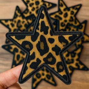 Peut inclure: Écussons en forme d'étoile avec un motif léopard. Les écussons présentent un fond beige avec des taches noires et une bordure noire cousue. Ces écussons peuvent être utilisés pour décorer des vêtements ou des accessoires.