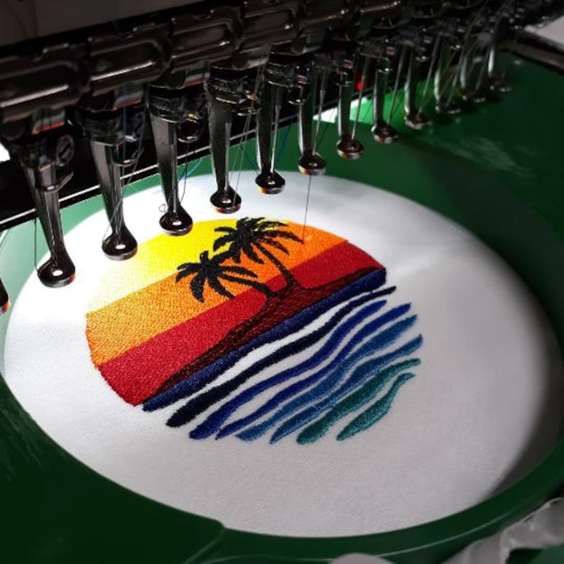 K&ouml;nnte beinhalten: Eine Stickmaschine in Betrieb, die eine Sonnenuntergangsszene mit Palmen und Meereswellen stickt. Das Design zeigt leuchtende Farben von Gelb, Orange, Rot, Blau und Gr&uuml;n auf einem wei&szlig;en Stoff.