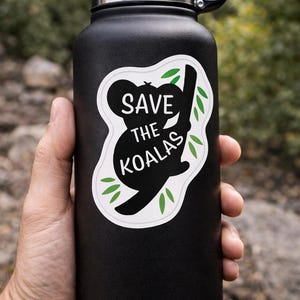 May include: Black insulated water bottle with a black lid and handle. A white sticker on the bottle features a black koala bear silhouette with the words "SAVE THE KOALAS" in white and green leaves.