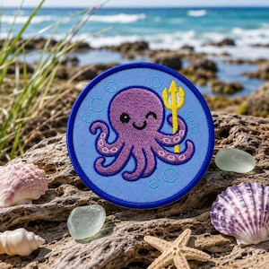 May include: A circular embroidered patch featuring a purple octopus with a smiling face and a winking eye. The octopus holds a yellow trident in one tentacle. The background is light blue with stitched circular bubbles in a darker blue.