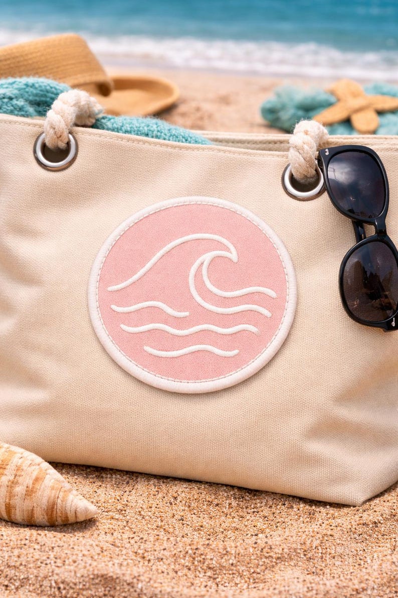 Peut inclure: Sac fourre-tout en toile beige avec un &eacute;cusson circulaire rose repr&eacute;sentant un motif de vagues blanches. Le sac a des poign&eacute;es en corde et des &oelig;illets m&eacute;talliques. Des lunettes de soleil sont pos&eacute;es sur le sac. Th&egrave;me plage.