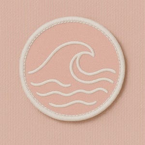 Peut inclure: Un &eacute;cusson rond rose avec un motif de vague blanc brod&eacute;. L'&eacute;cusson a une bordure blanche et est pos&eacute; sur un fond rose textur&eacute;. Le motif de la vague pr&eacute;sente une grande vague d&eacute;ferlante et trois vagues plus petites.