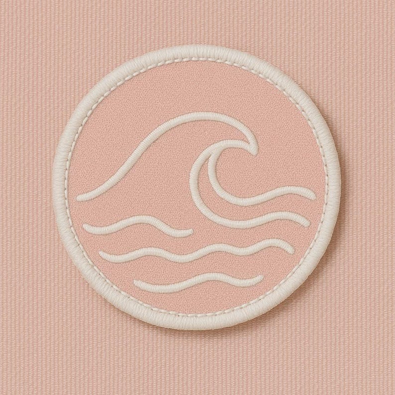 Peut inclure: Un &eacute;cusson rond rose avec un motif de vague blanc brod&eacute;. L'&eacute;cusson a une bordure blanche et est pos&eacute; sur un fond rose textur&eacute;. Le motif de la vague pr&eacute;sente une grande vague d&eacute;ferlante et trois vagues plus petites.