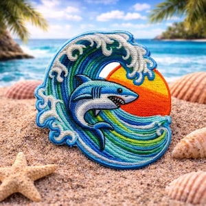 May include: Embroidered patch featuring a blue and white shark leaping from a wave. The wave is blue, green, and white, with a yellow and orange sunset in the background. The patch is on a sandy beach with seashells and a starfish.