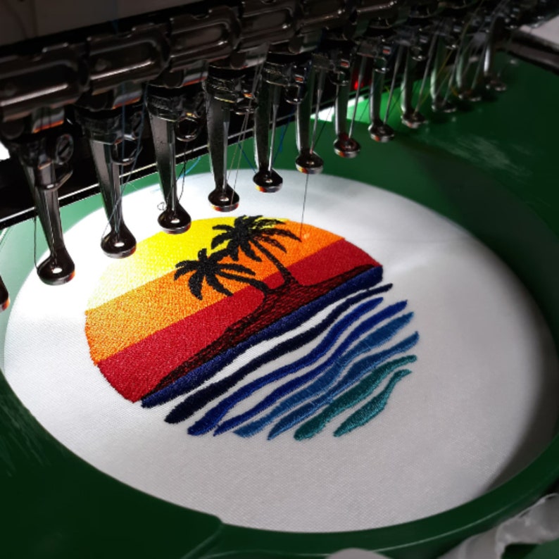 May include: Close-up of a white embroidery hoop with a colorful embroidered design of a sunset with palm trees and ocean waves.
