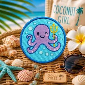 May include: A round, embroidered patch featuring a purple octopus with a golden trident, set against a light blue background with bubbles. The patch is surrounded by a darker blue border. The patch is on a woven surface with seashells and a wooden sign that says "GOOD VIBES".