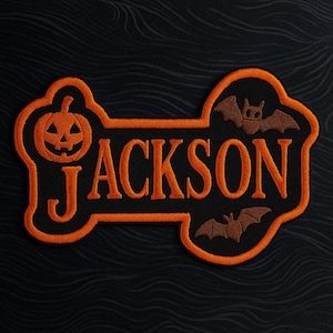 May include: Embroidered patch in the shape of a bone, with the name "JACKSON" in orange letters. A jack-o'-lantern and two bats are also featured. The patch has an orange border and is set against a black background.