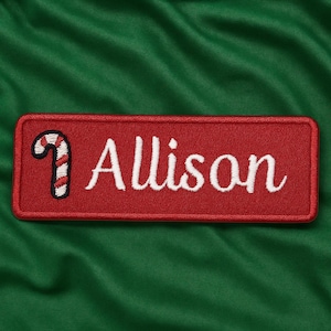 May include: A red rectangular patch with the name "Allison" embroidered in white script. A candy cane graphic is in the upper left corner. The patch is set against a green fabric background.