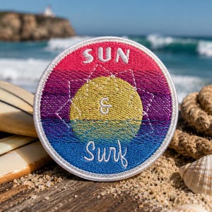 以下が含まれることがあります： 「SUN & SURF」の文字が刺繍された丸いパッチ。ピンク、黄色、紫、青の鮮やかなグラデーションデザイン。サーフボード、砂浜、海の背景に配置されています。パッチには白い縁取りがあります。