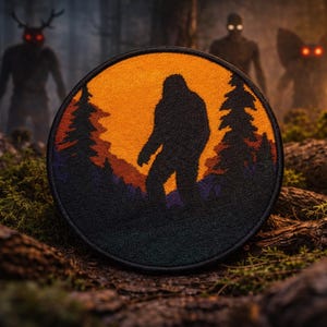 Op de afbeelding: Ronde patch met een silhouet van Bigfoot voor een zonsondergang met bomen. De patch is zwart met oranje, paarse en groene accenten. De achtergrond toont drie schimmige figuren met gloeiende ogen in een bos.