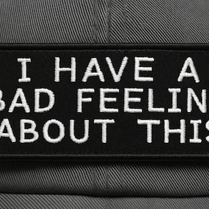 May include: A grey baseball cap with a black rectangular patch. The patch has the white embroidered text: "I HAVE A BAD FEELING ABOUT THIS". The cap is made of a durable fabric.