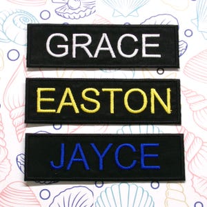 May include: Three black fabric patches with white, yellow, and blue embroidered lettering. The patches read "GRACE", "EASTON", and "JAYCE".