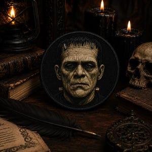 May include: A circular embroidered patch featuring a detailed portrait of Frankenstein's monster with pale green skin, a prominent forehead scar, and metallic neck bolts. The design is rendered in shades of green, black, and grey with a black border.