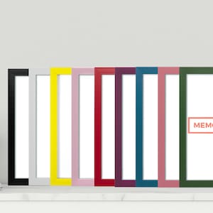 May include: Ten picture frames, all the same size, are lined up on a white shelf. The frames are black, white, yellow, pink, red, purple, blue, light pink, green, and have a white mount. The frame on the far right has the words "MEMORY BOX" printed in orange on the mount.