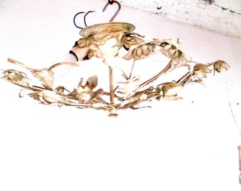 Könnte beinhalten: Ein antiker Kronleuchter mit floralem Design. Die Leuchte ist aus Metall gefertigt und hat eine cremefarbene Oberfläche mit braunen Akzenten. Der Kronleuchter wird mit einem Haken an der Decke befestigt.