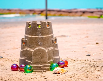 May include: A sandcastle on a beach with colorful marbles and a seashell.