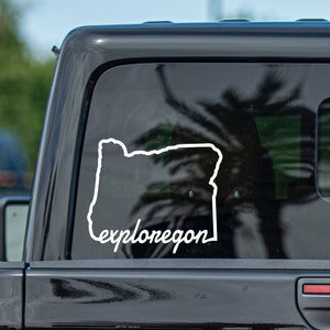 May include: A white vinyl sticker on a black car window. The sticker features an outline of the state of Oregon with the text "explore oregon" underneath.