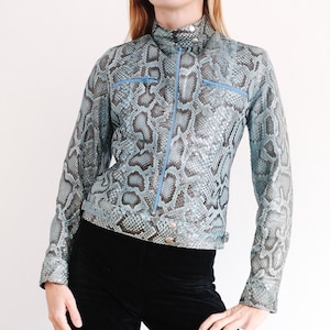 Op de afbeelding: Een blauw slangenleren jack met een ritssluiting en een opstaande kraag. Het jack heeft twee zakken aan de voorkant en lange mouwen.