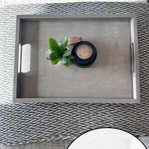 May include: A weathered gray wooden tray with a small plant and a candle in a black jar. The tray has two handles on the sides.