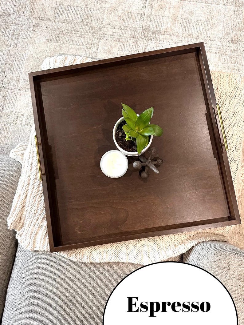 K&ouml;nnte beinhalten: Serviertablett aus Espresso-Holz mit goldenen Griffen. Das Tablett ist leer und hat eine kleine Pflanze und eine Kerze darauf.