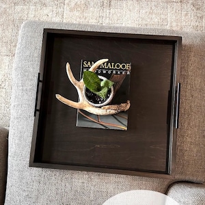 May include: A dark brown wooden tray with a black frame, featuring a small potted plant and a set of antlers. The tray is labeled "Sam Maloof Woodworker".