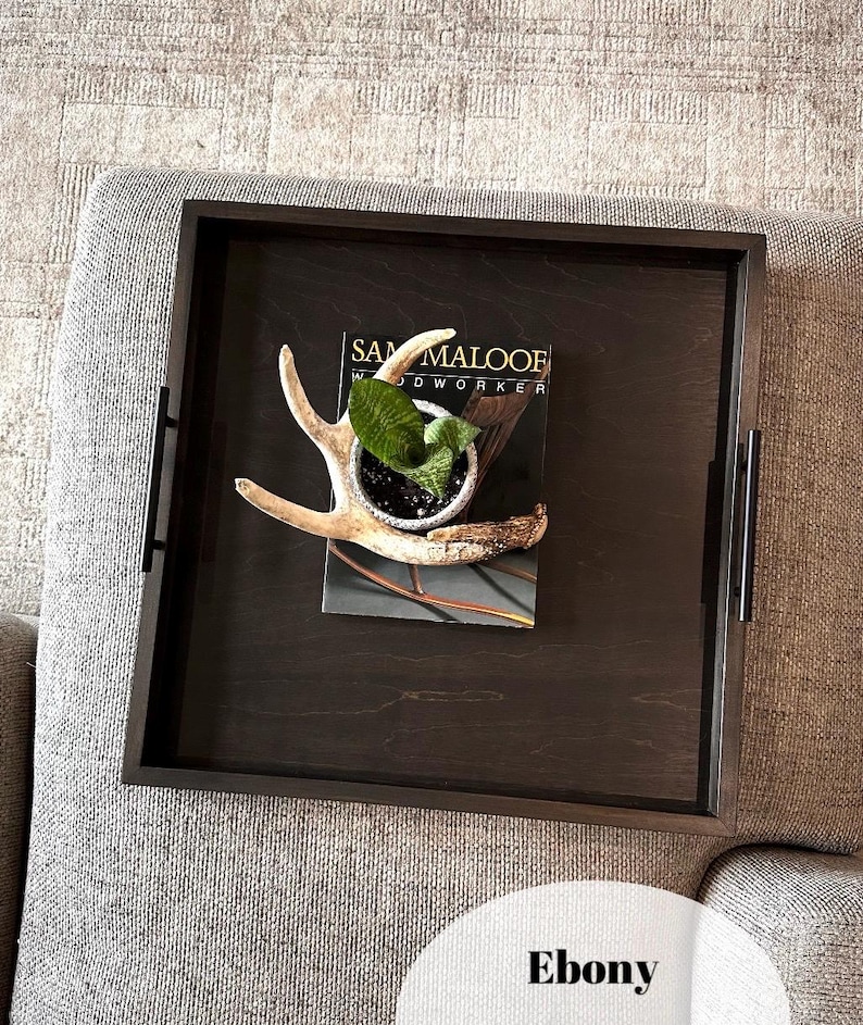 May include: A dark brown wooden tray with a black frame, featuring a small potted plant and a set of antlers. The tray is labeled "Sam Maloof Woodworker".