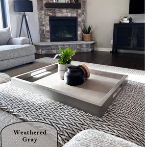 May include: A weathered gray rectangular serving tray with rounded corners and two handles on the sides. The tray is sitting on a black and white patterned throw blanket.