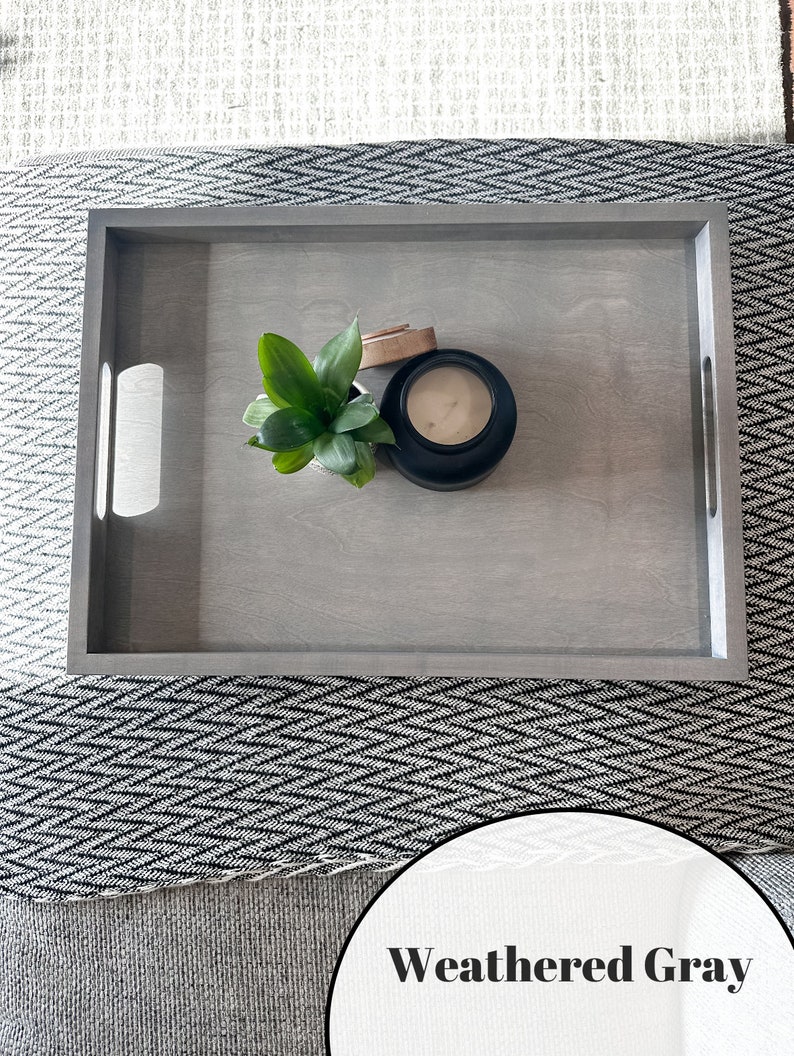 K&ouml;nnte beinhalten: Ein verwittertes graues Holztablett mit einer kleinen Pflanze und einer Kerze in einem schwarzen Glas. Das Tablett hat zwei Griffe an den Seiten.