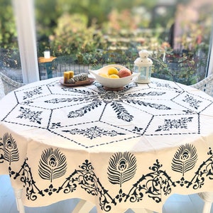 May include: A white tablecloth with a black and white geometric pattern and peacock feather design. The tablecloth is round and has a diameter of approximately 120 cm.